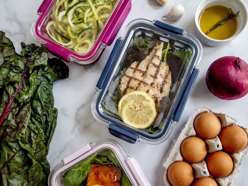 Healthy meal prep containers with grilled chicken, greens, and fresh vegetables